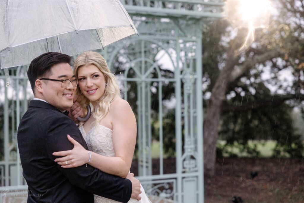 Bride and Groom under a clear umbrella on their rainy wedding day at Ma Maison, an Austin Wedding venue