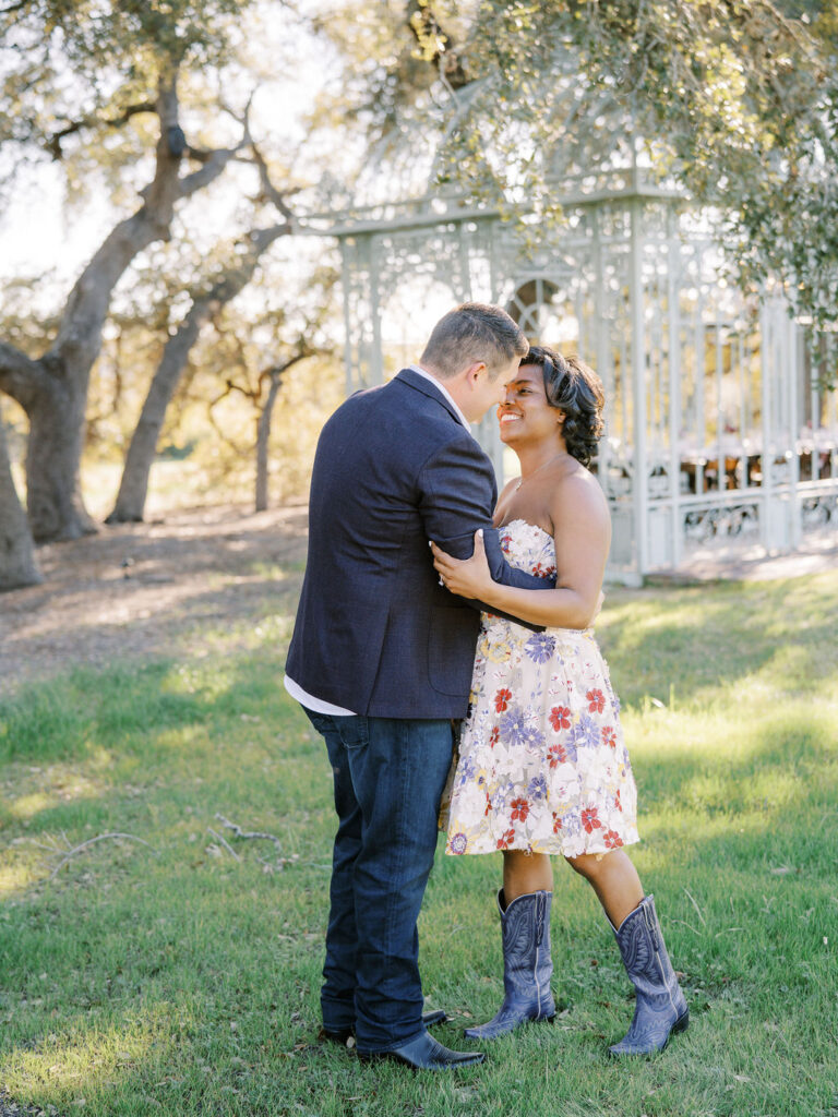 A couple smiles at each other near a gazebo, capturing Engagement Party Etiquette in 2026