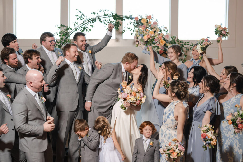 Joyful wedding party celebrating the couple’s kiss, capturing 2026 wedding trends