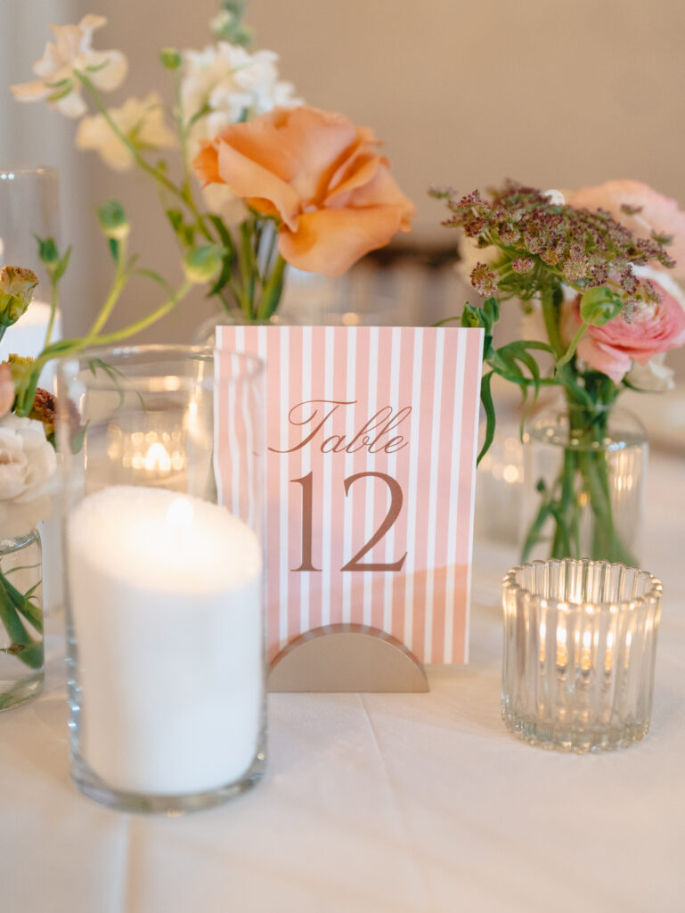 Pink striped table number 12 surrounded by flowers and candles.