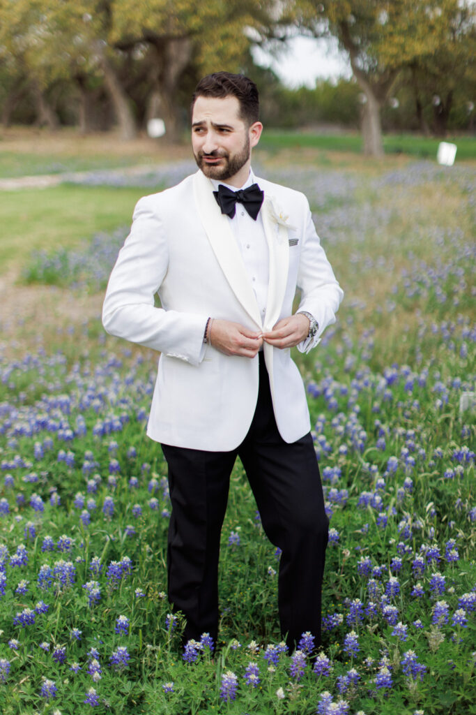 groom buttoning jacket in wildflower field