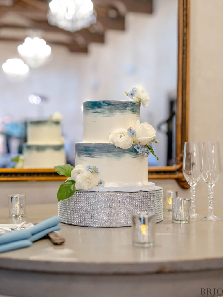 blue and white wedding cake with glassware surrounding it