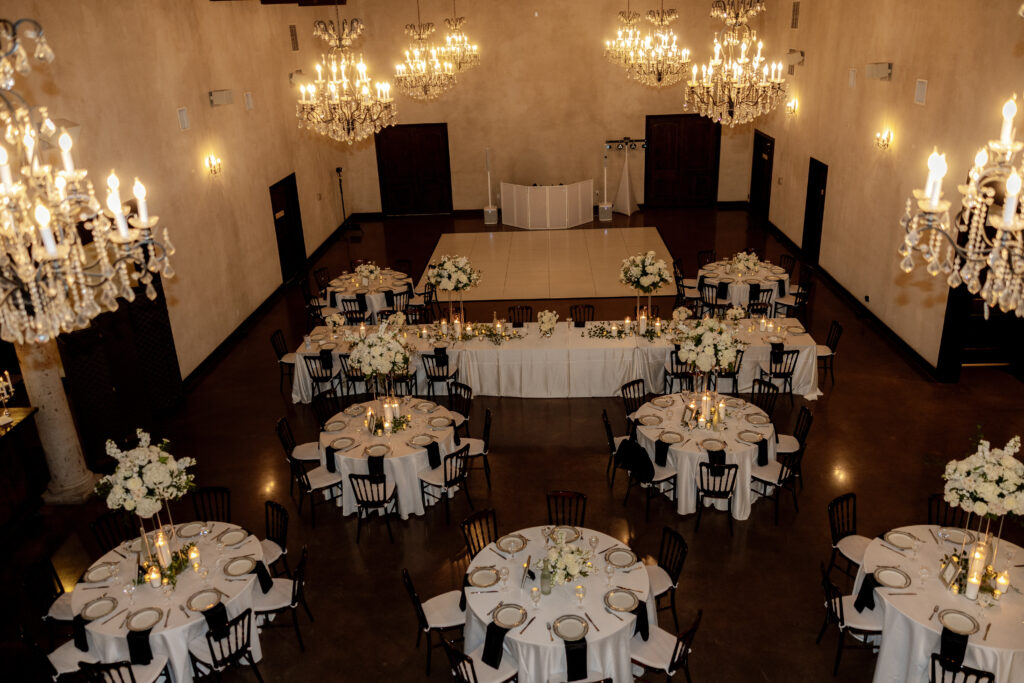 Elegant wedding reception ballroom with white florals, chandeliers, and a dance floor.