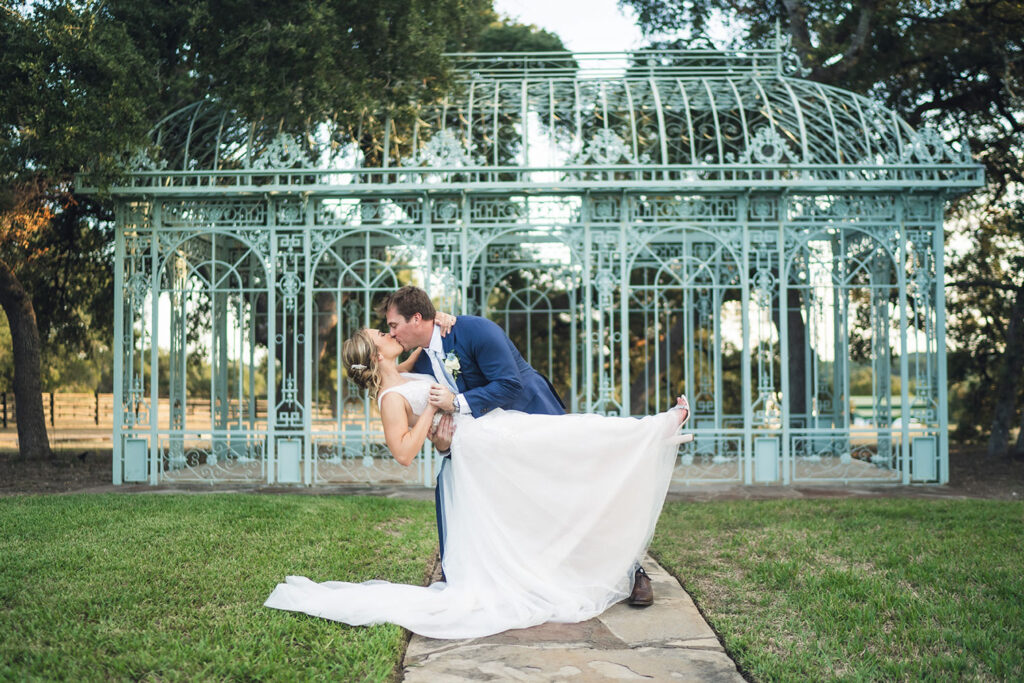 A groom dips his bride for a kiss in front of Ma Maison’s stunning Green Cathedral, a cinematic shot for an Austin videographer.