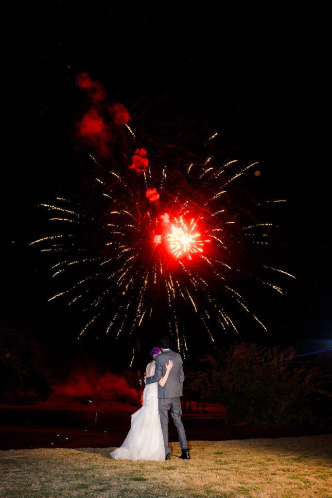 A couple embraces under a sky lit with red fireworks, a magical moment documented by an Austin wedding videographer