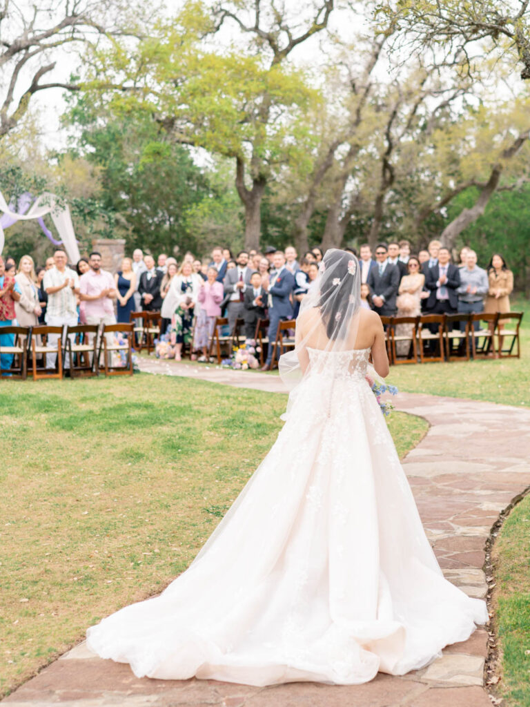 A breathtaking moment as the bride walks towards her groom under the canopy of Texas oaks, filmed by an Austin videographer.