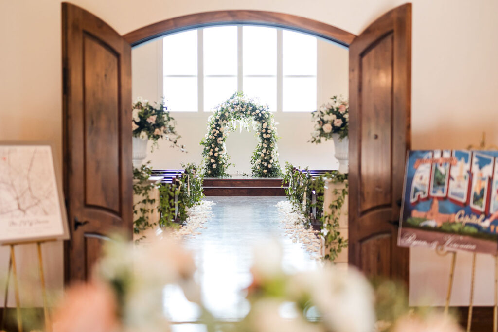 A beautifully decorated indoor wedding ceremony at Ma Maison, featuring a stunning floral arch and greenery-lined aisles.