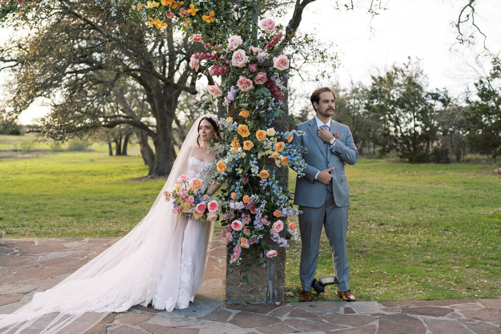 A bride and groom stand on either side of a vibrant floral pillar at Ma Maison, a stunning Austin wedding venue.