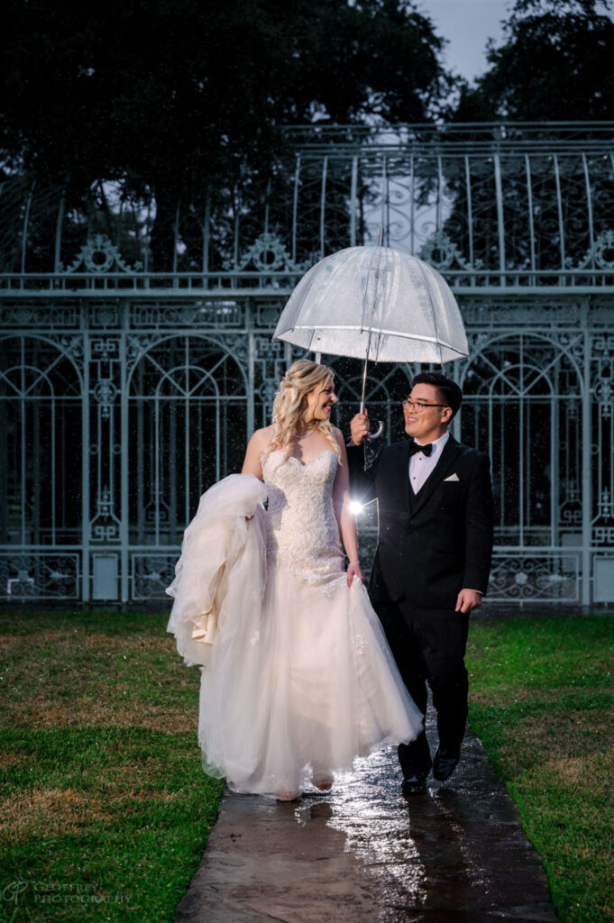 A bride and groom embrace under an umbrella at Ma Maison’s Green Cathedral, capturing the beauty of a rainy wedding.