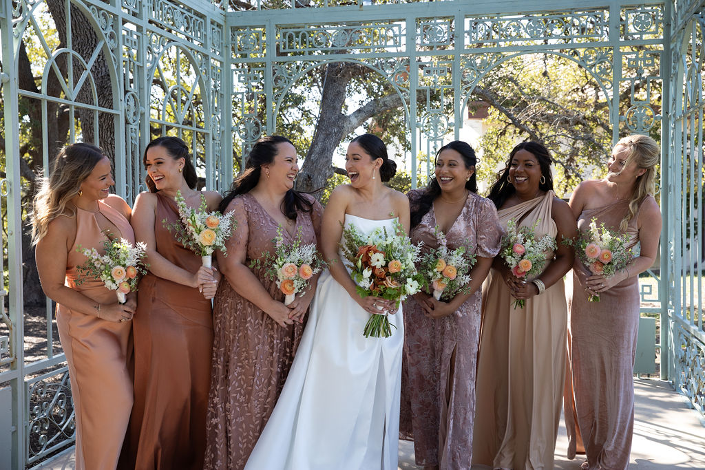 Bride with bridesmaids in coordinated gowns holding bouquets at black-tie wedding