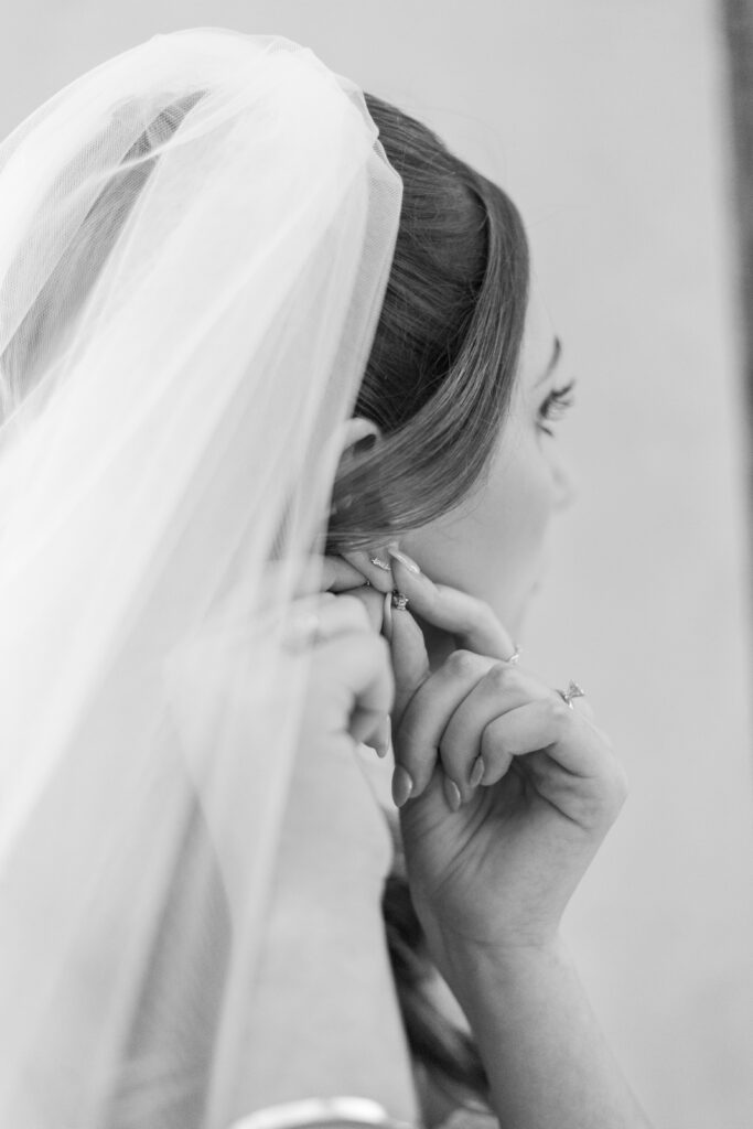 Bride putting on earrings beneath her wedding veil