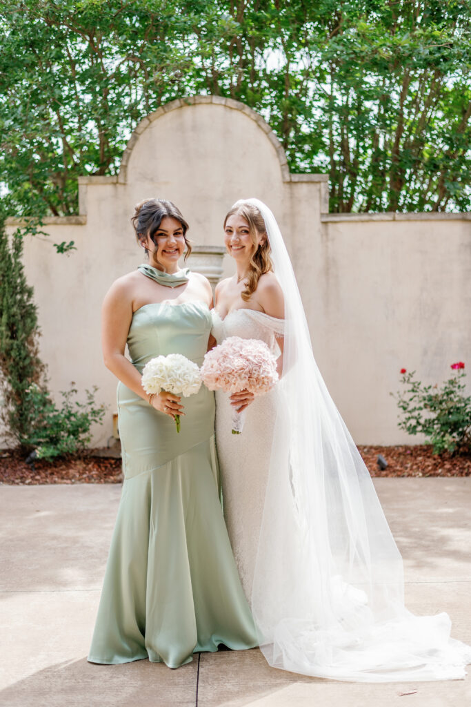 Bride posing with bridesmaid in a sage green dress and bouquets.