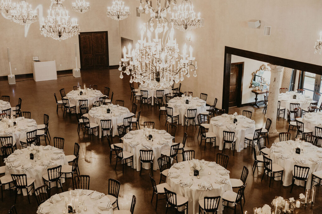 Elegant indoor reception setup with round tables and chandeliers at Ma Maison, a luxury venue that offers budget-friendly wedding packages in Austin, Texas.