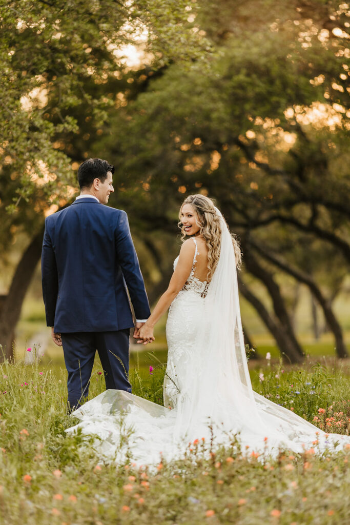 Bride and groom holding hands and smiling in a wildflower field at a Dallas wedding venue