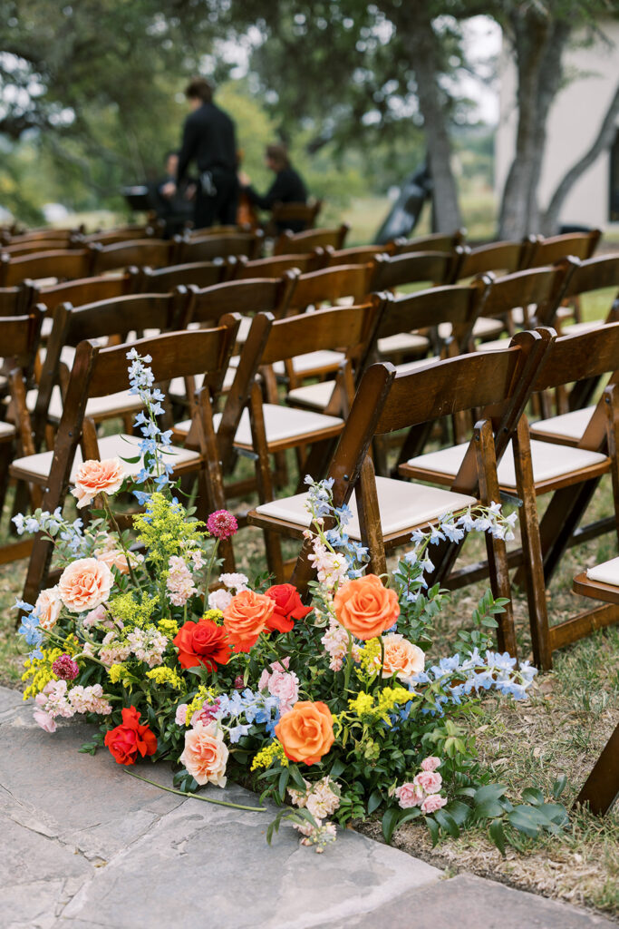 Vibrant wedding aisle flowers beside rows of wooden ceremony chairs.