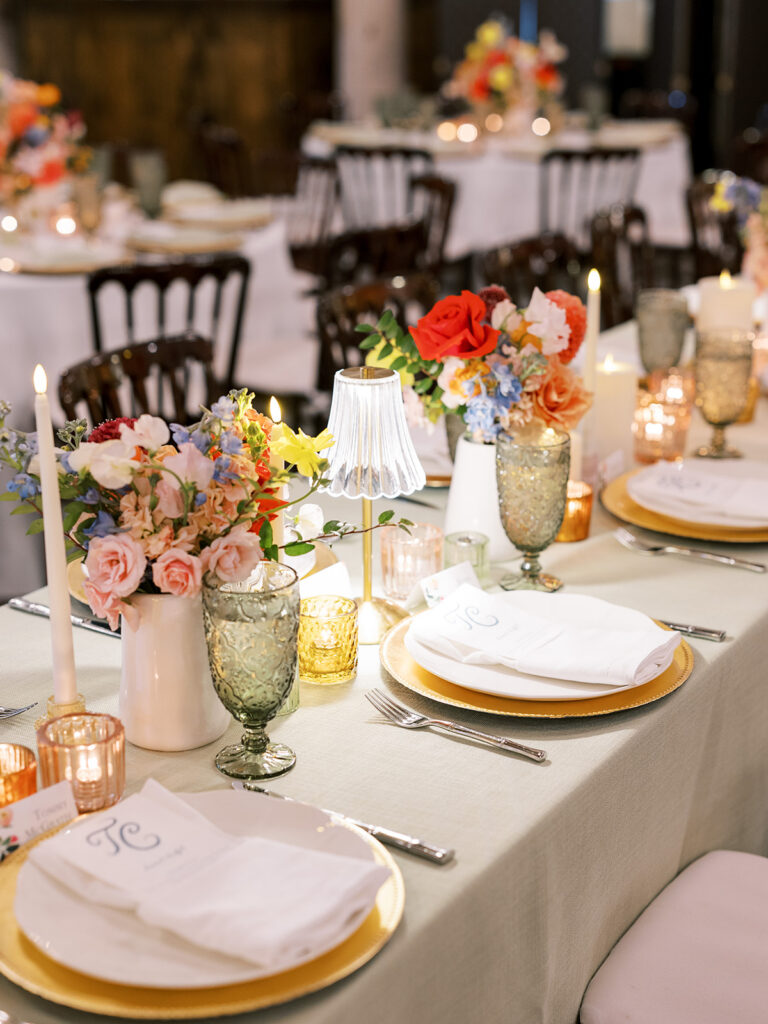 Elegant wedding table setting with colorful flowers, candles, and gold-rimmed plates.