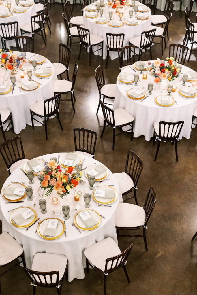 Round wedding reception tables with colorful floral centerpieces and gold place settings.