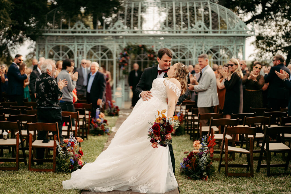 Newlyweds dipping kiss in aisle surrounded by guests