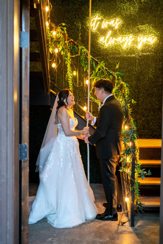 Couple ringing the Ma Maison love bell beneath string lights and greenery