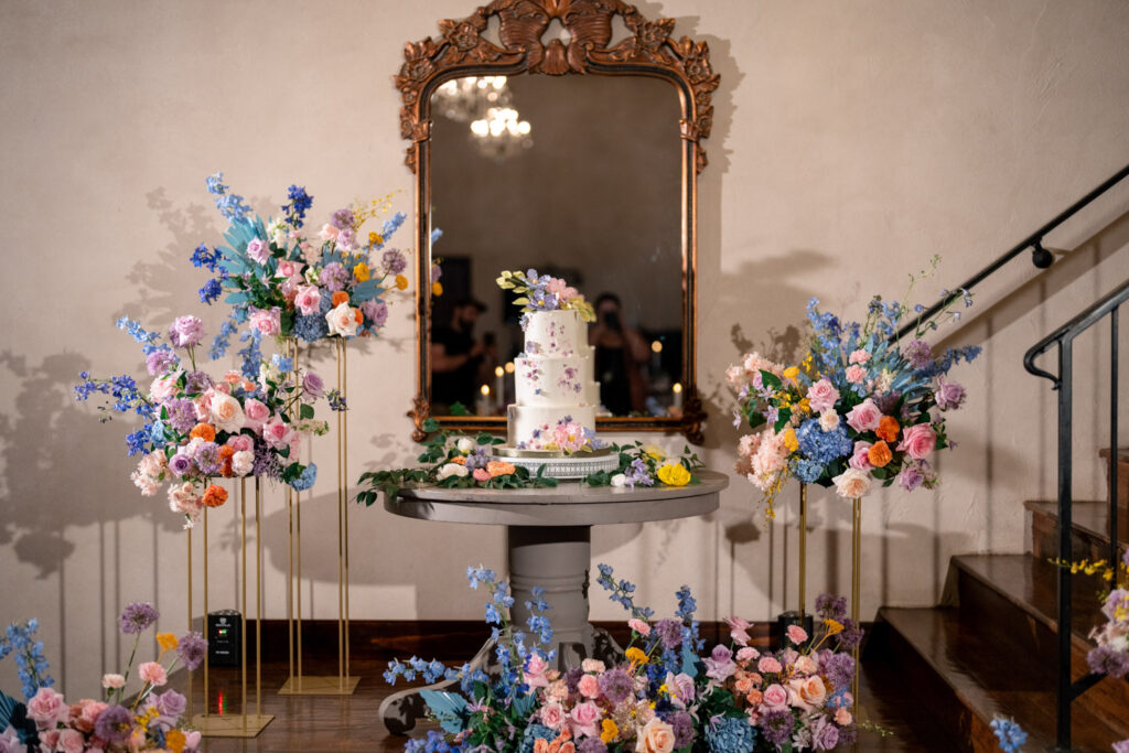 Pastel floral wedding cake display surrounded by European-inspired arrangements at Ma Maison