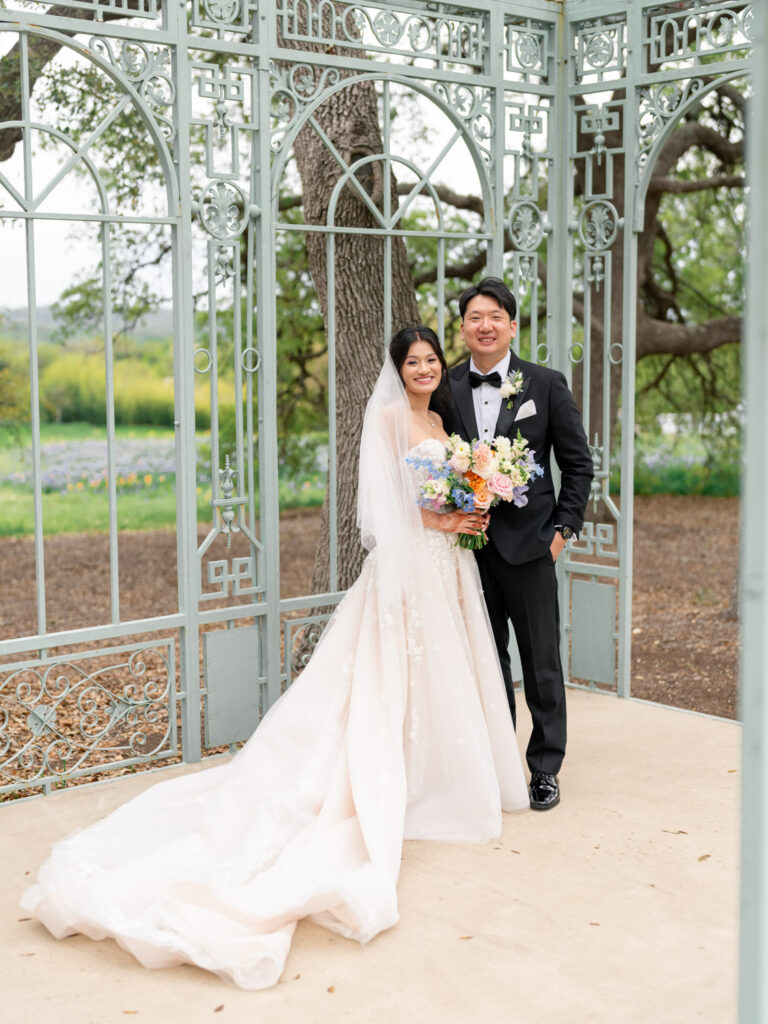Bride and groom standing inside the Ma Maison iron gazebo with floral bouquet