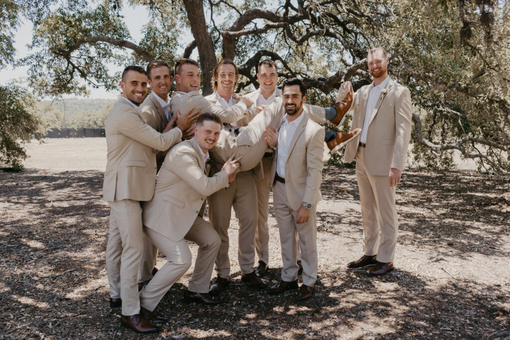 Groomsmen lifting groom outdoors