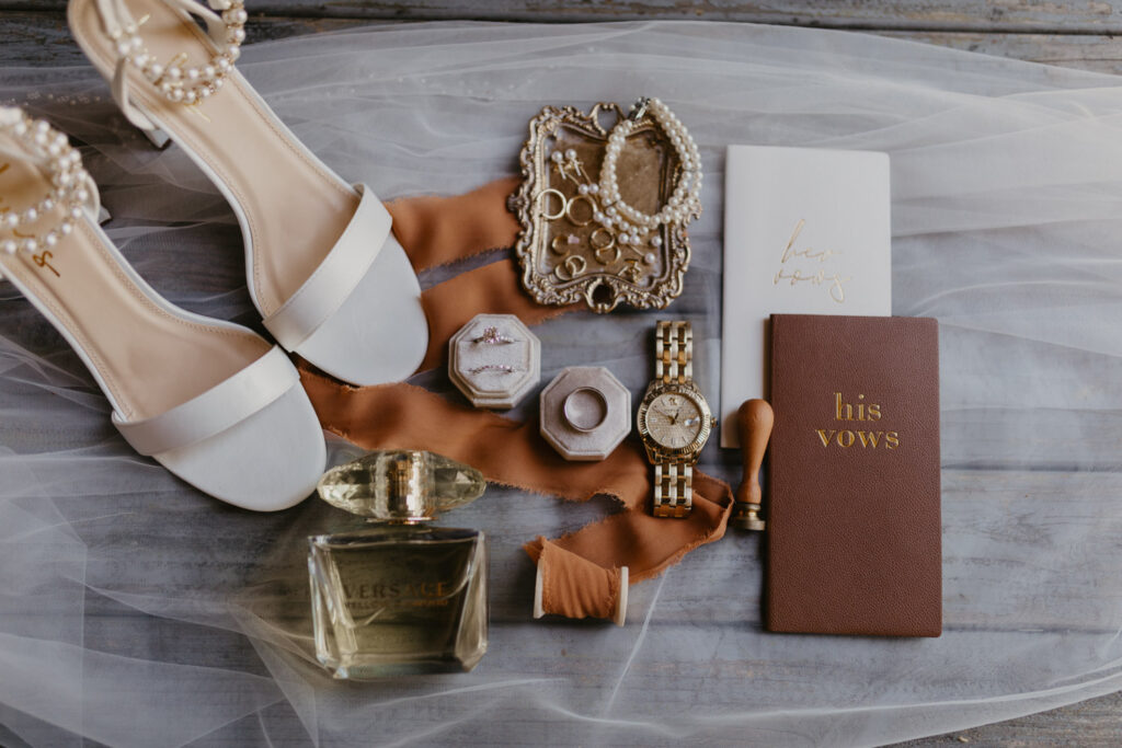 Flat lay of wedding details with shoes jewelry and vow books