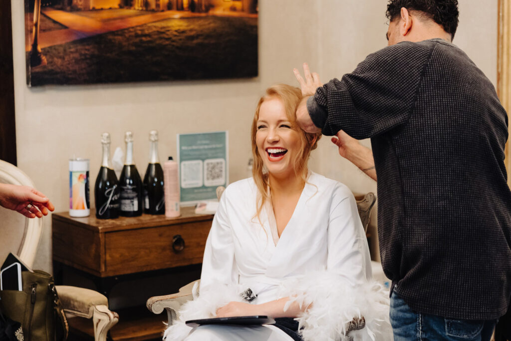 Bride laughing joyfully during hair styling by a professional wedding hair and makeup artist in Austin’s elegant bridal suite.