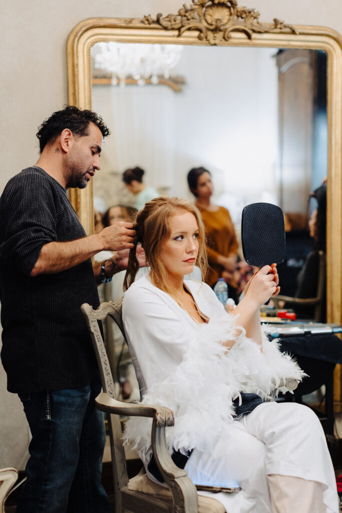 Bride checking her hairstyle in the mirror while a hair and makeup artist in Austin perfects her wedding day look.