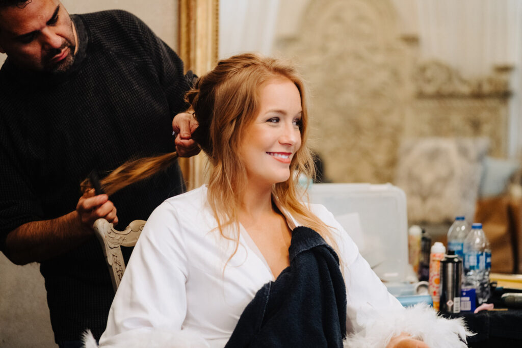 Bride smiling during final touch-ups by a skilled hair and makeup artist in Austin before her wedding ceremony.