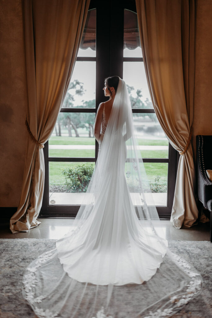 Bride gazing out window in her wedding gown and veil at Italian-inspired venue in Austin, TX.