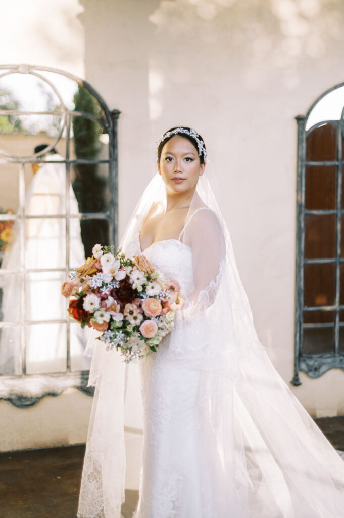 A radiant bride poses with her bouquet in front of a rustic window at Ma Maison