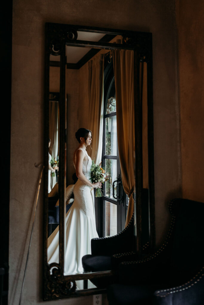 A bride gazes out a grand arched window at Ma Maison