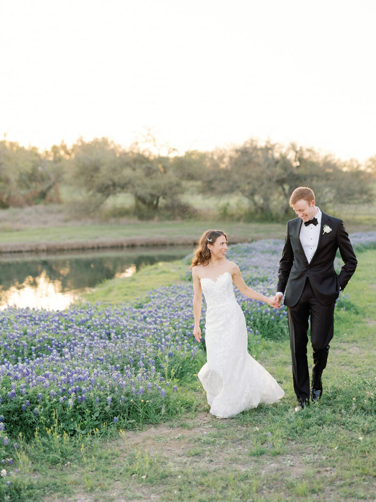 bride and groom walking alongside lake with wildflowers in the background