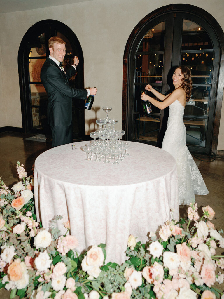 bride and groom popping champagne next to a champagne tower