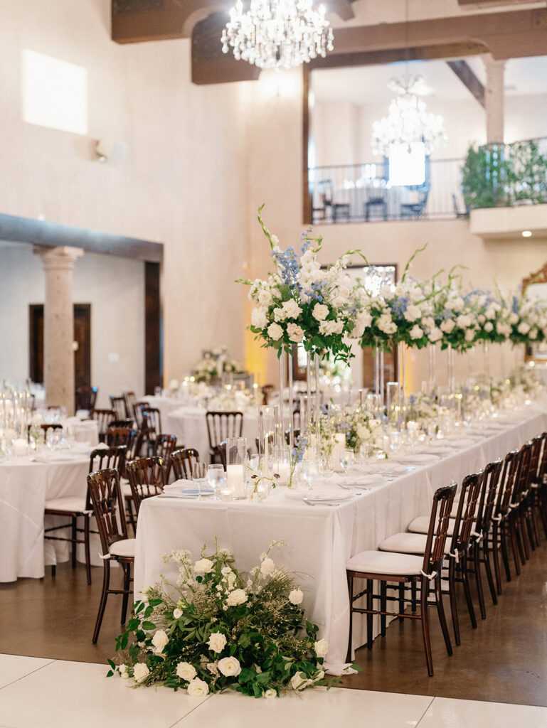 Elegant wedding reception table with white and blue floral centerpieces and crystal chandeliers.