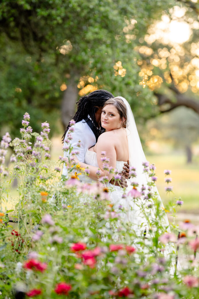 A newlywed couple shares a tender moment among colorful garden flowers
