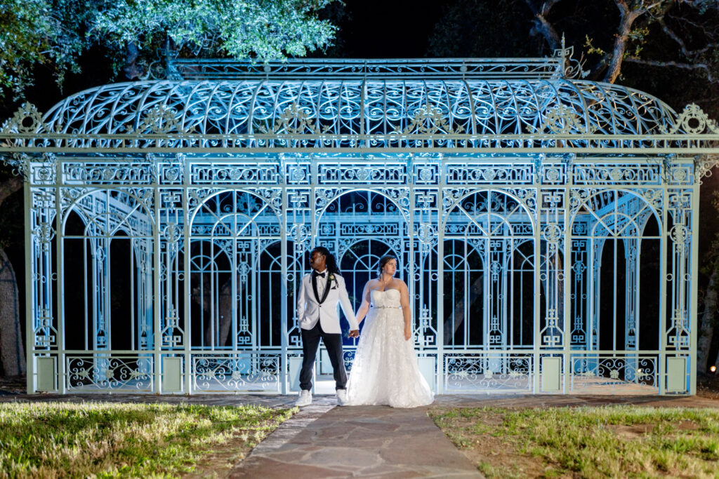 The couple holds hands in front of Ma Maison’s illuminated iron pavilion at night