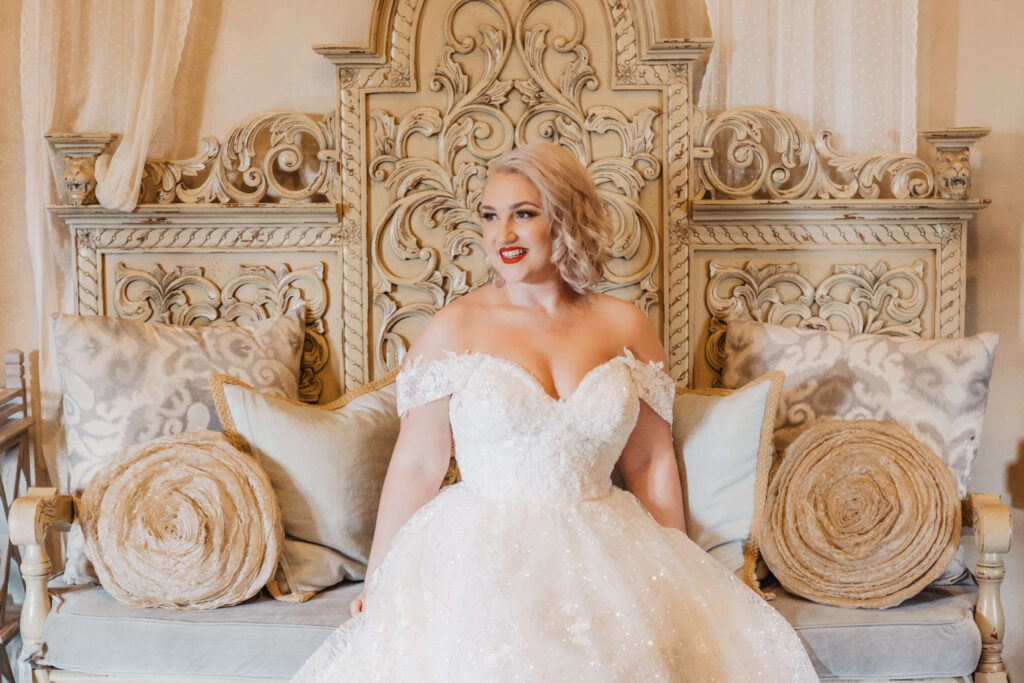 bride sitting on beautiful bench with throw pillows on her wedding day