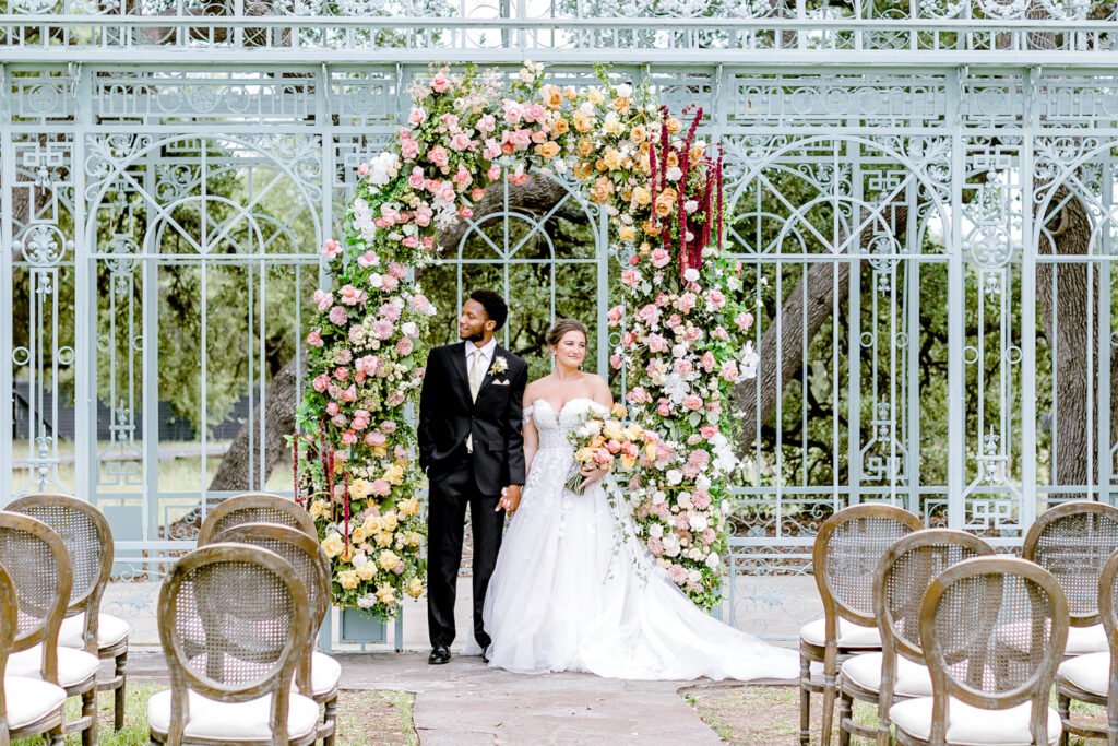 bride and groom standing in front of floral arch at wedding ceremony