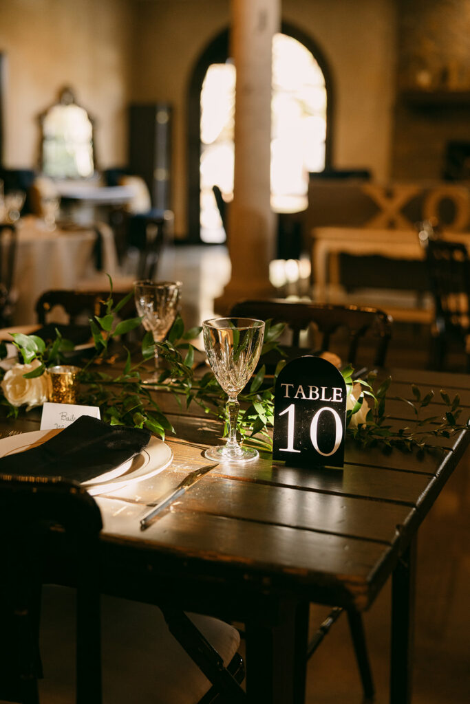 Rustic wedding table setting with greenery, glassware, and table number 10.