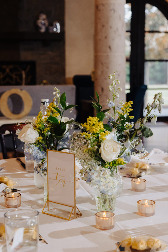 White and yellow wedding floral centerpiece with candles and table number sign.