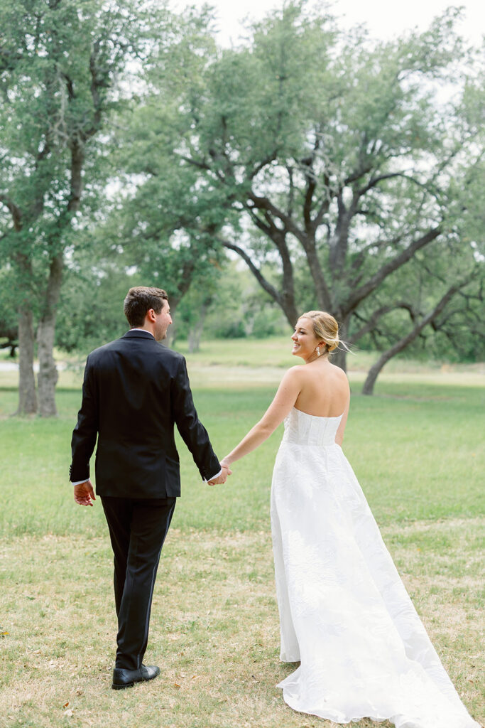 Bride and groom walking hand in hand through a scenic outdoor wedding venue.