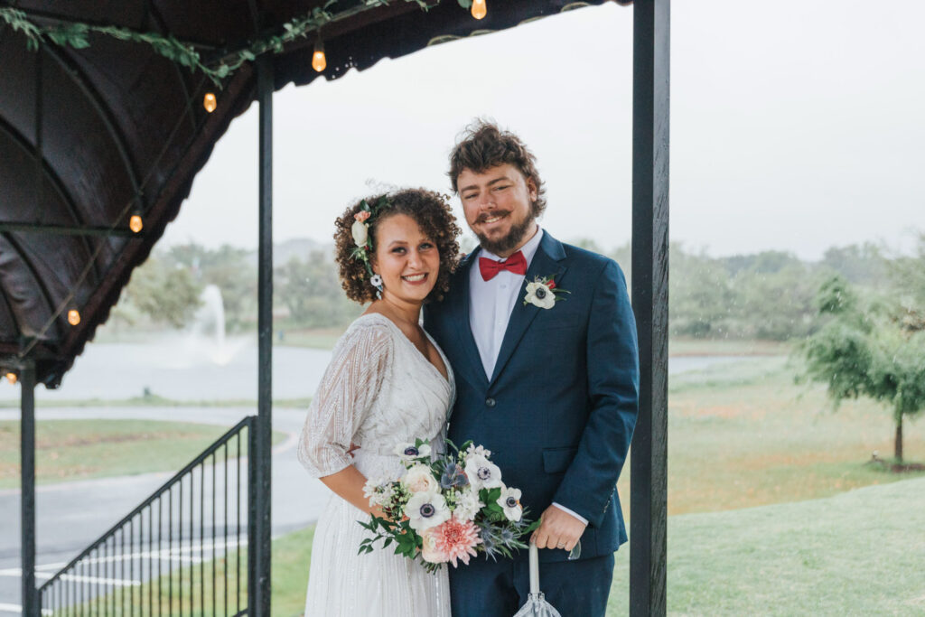 Smiling couple pose with bouquet on a rainy wedding day