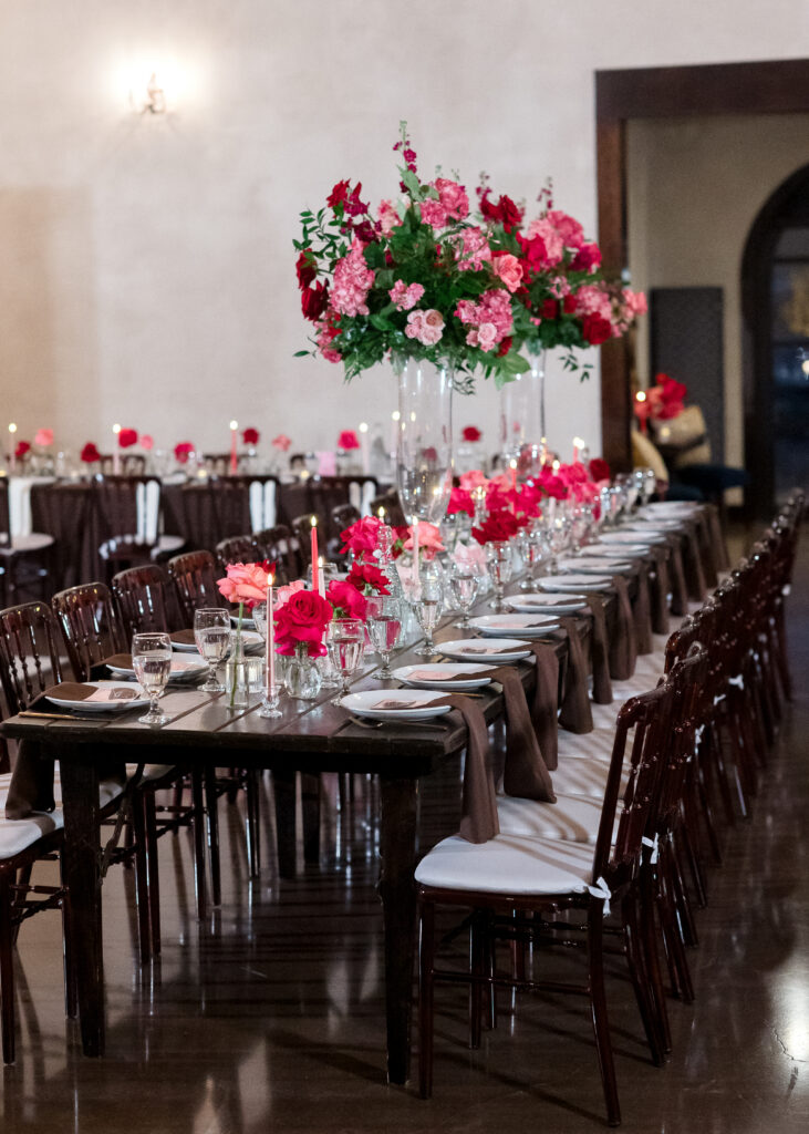Long reception table with vibrant pink floral centerpieces and elegant place settings.