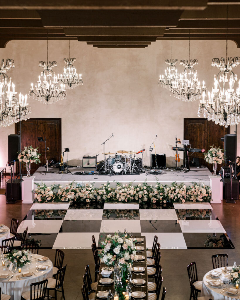 Elegant grand ballroom at Ma Maison with a checkered dance floor surrounded by beautifully arranged guest tables and chandeliers.