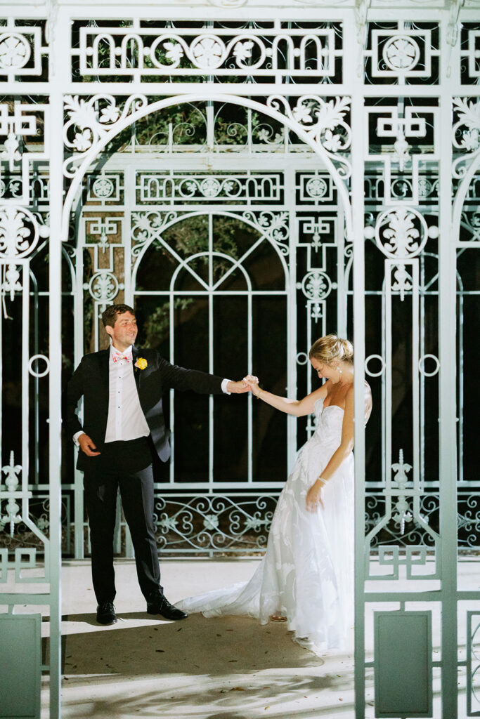 Bride and groom holding hands inside an ornate greenhouse wedding venue.