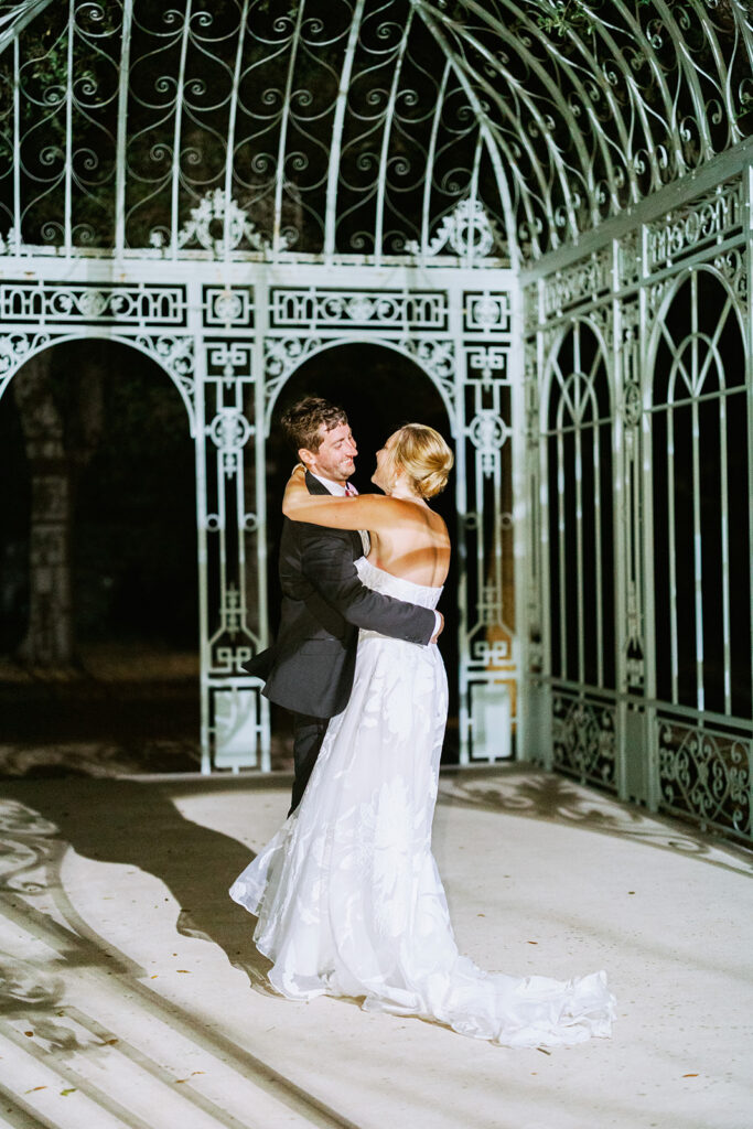 Bride and groom embracing inside a decorative glass greenhouse.