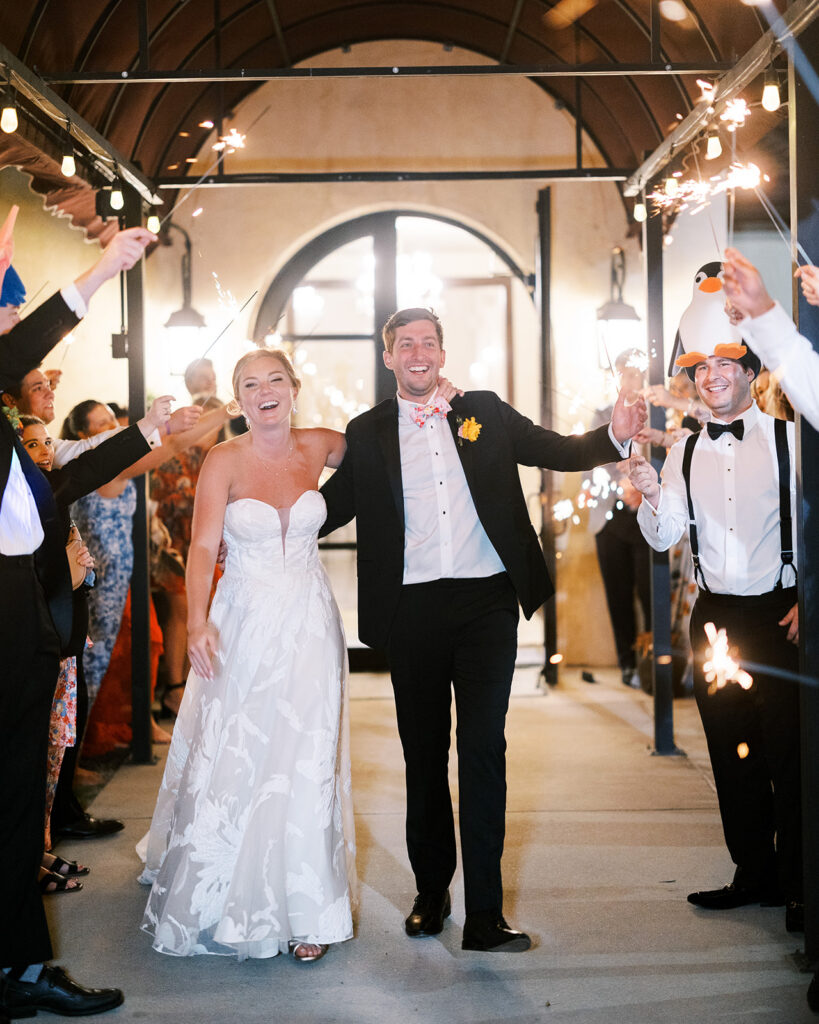Newlyweds walking through a sparkler exit with wedding guests cheering.
