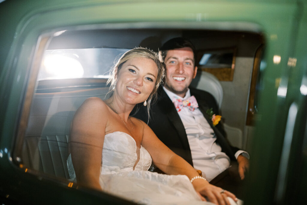 Bride and groom smiling together inside their wedding getaway car.